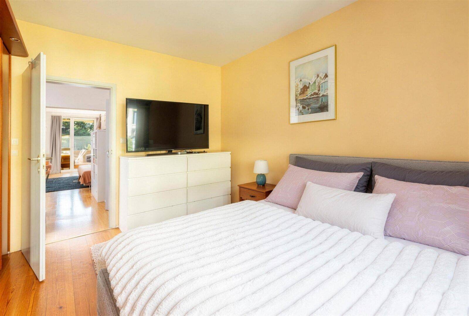 Schlafzimmer mit gelben Wänden, Fernseher auf Kommode und Zugang zu einem weiteren Raum.