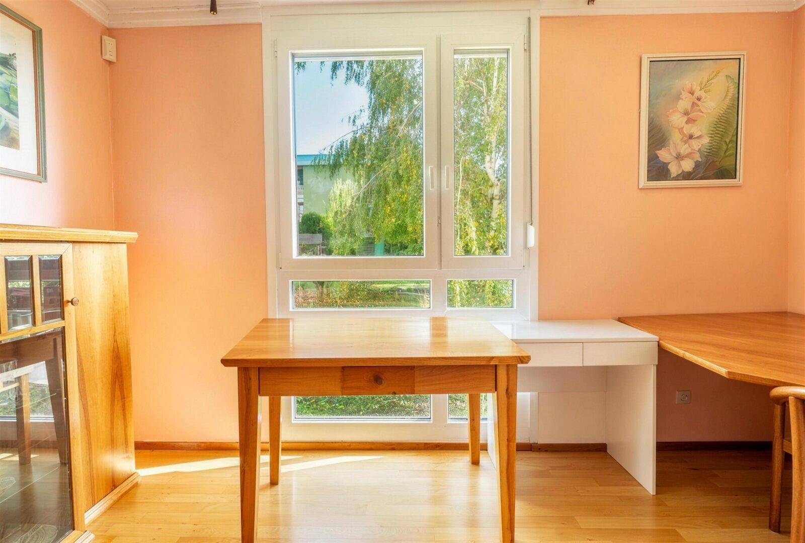 Heller Arbeitsbereich mit Schreibtisch vor großem Fenster und Blick ins Grüne.