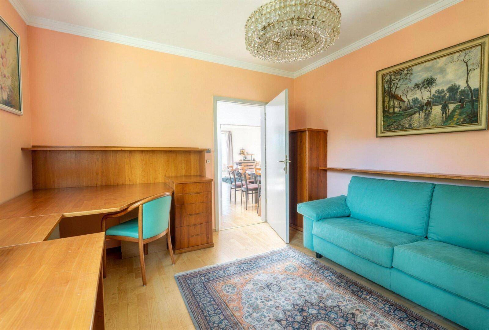 Arbeitszimmer mit Holzschreibtisch, Sofa und offenem Zugang zum Essbereich.