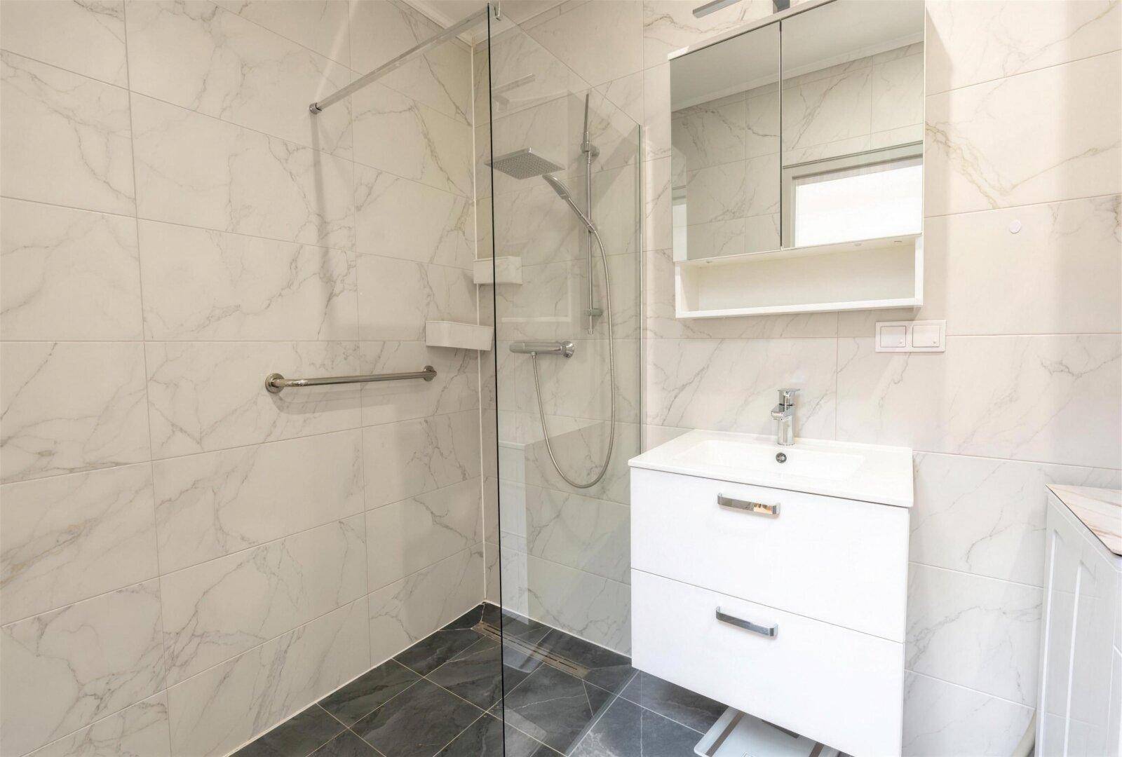 Modernes Badezimmer mit Marmorfliesen, ebenerdiger Dusche und Haltegriffen.