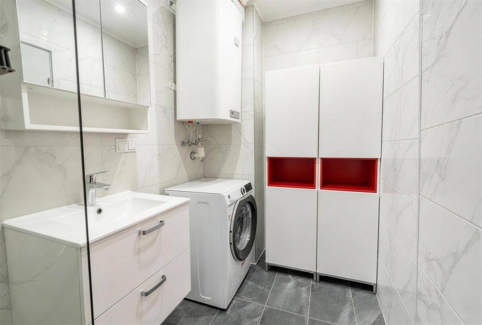 Badezimmer mit Waschmaschine, modernen Schränken und weiß-grauen Fliesen.