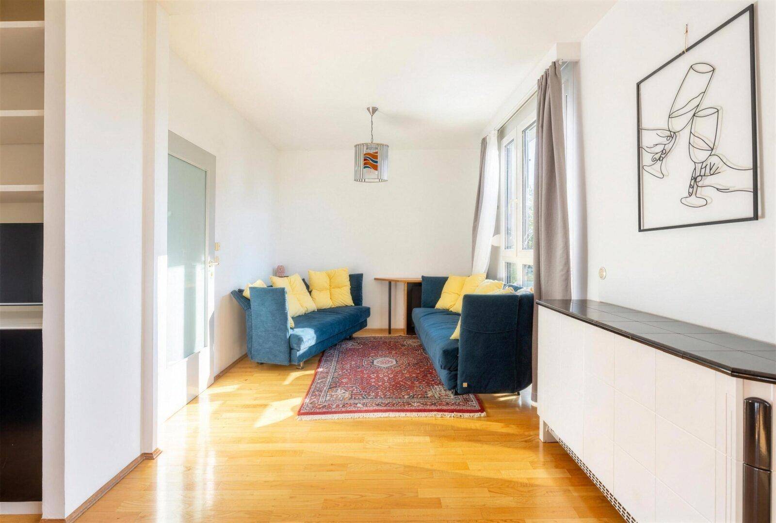 Gemütlicher Wohnbereich mit blauen Sofas, Teppich und großen Fenstern für viel Licht.