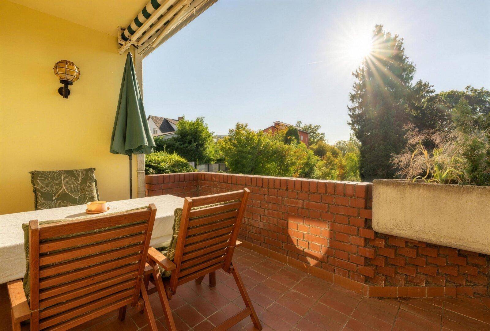 Sonniger Terrassenbereich mit Gartenmöbeln, Ziegelmauer und Blick ins Grüne.