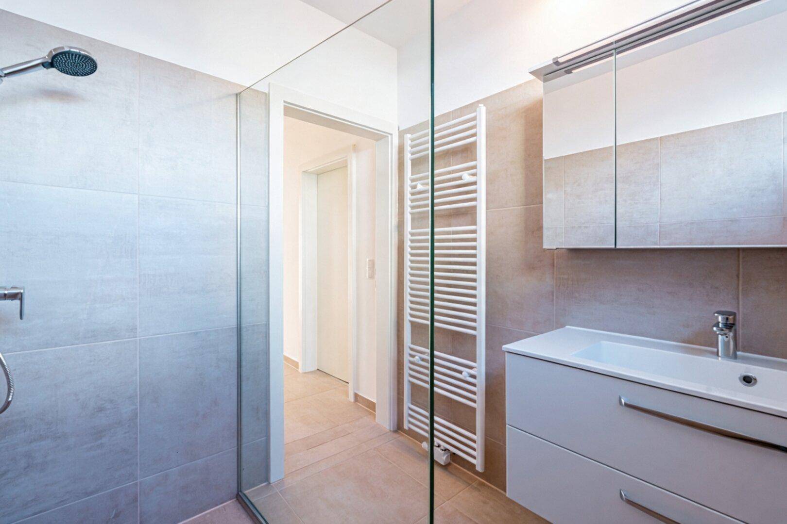 Helles Badezimmer mit großer ebenerdiger Dusche, Waschtisch und Spiegelschrank, modern gefliest.