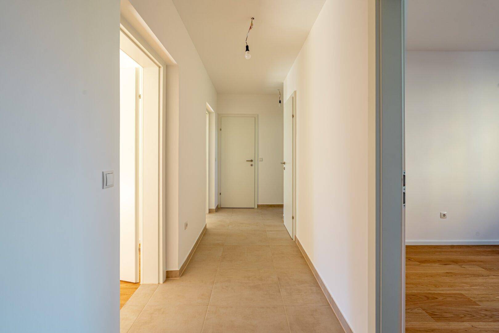 Geräumiger Flur mit Fliesenboden und weißen Wänden, der die verschiedenen Räume der Wohnung verbindet.