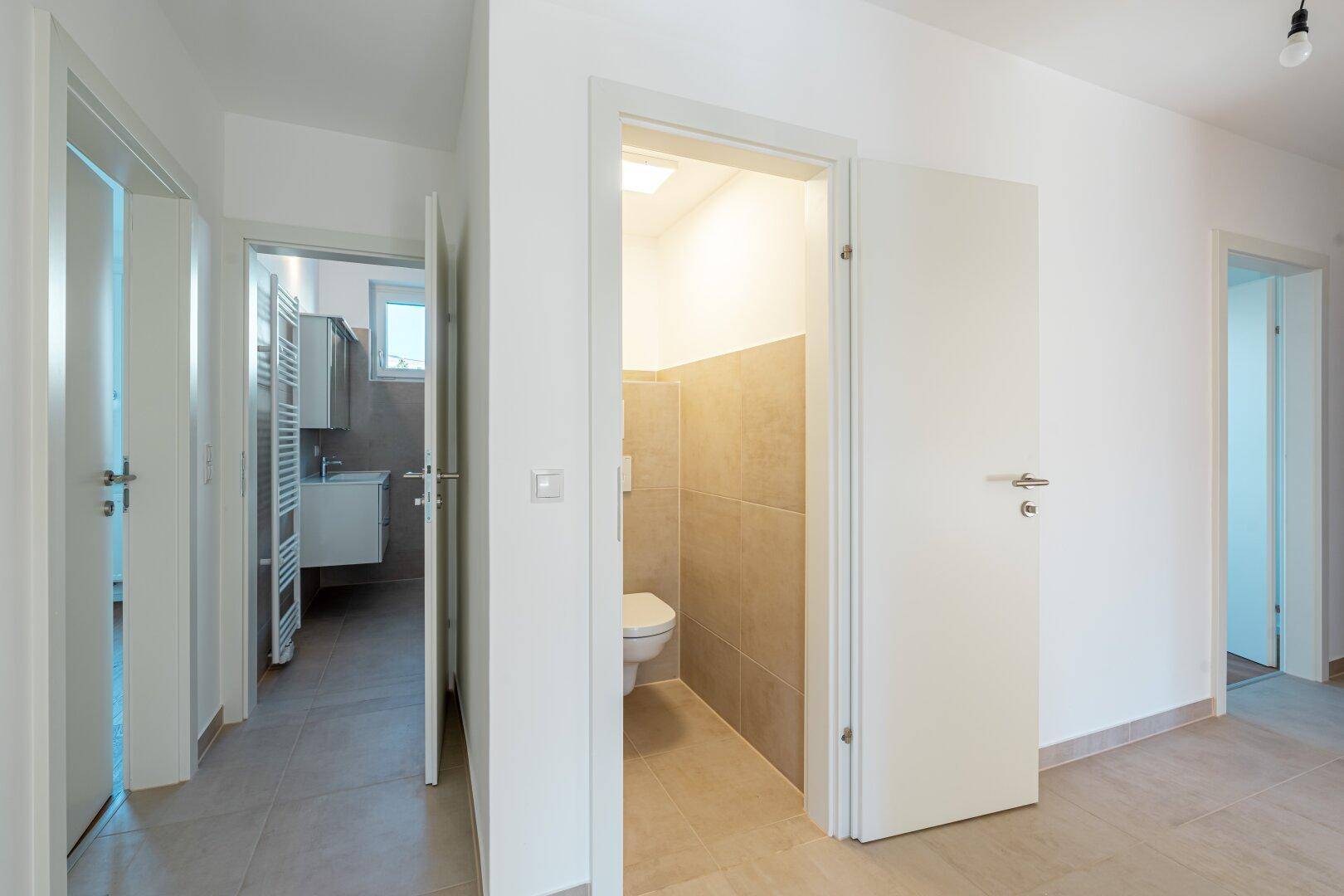 Heller Flur mit Fliesenboden, der Zugang zu einem separaten WC und einem weiteren Badezimmer bietet.