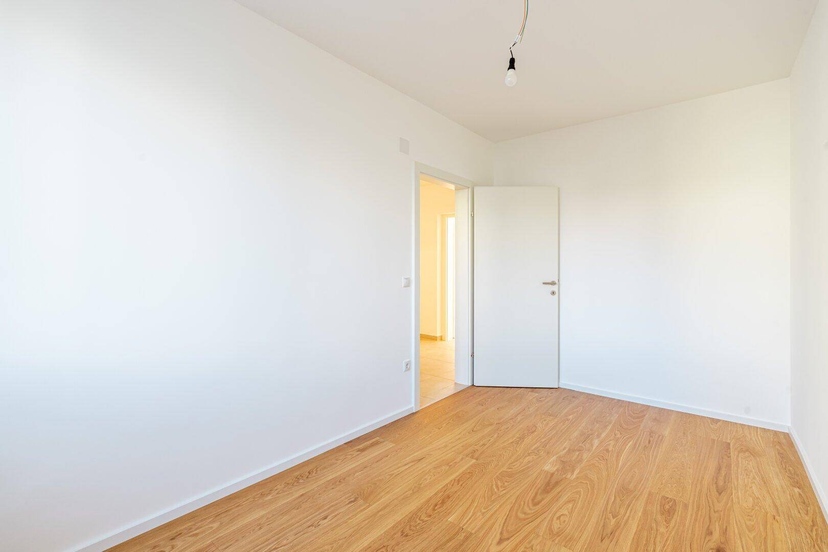 Leeres Zimmer mit hellem Holzfußboden und weiß gestrichenen Wänden, ideal als Kinder- oder Arbeitszimmer.