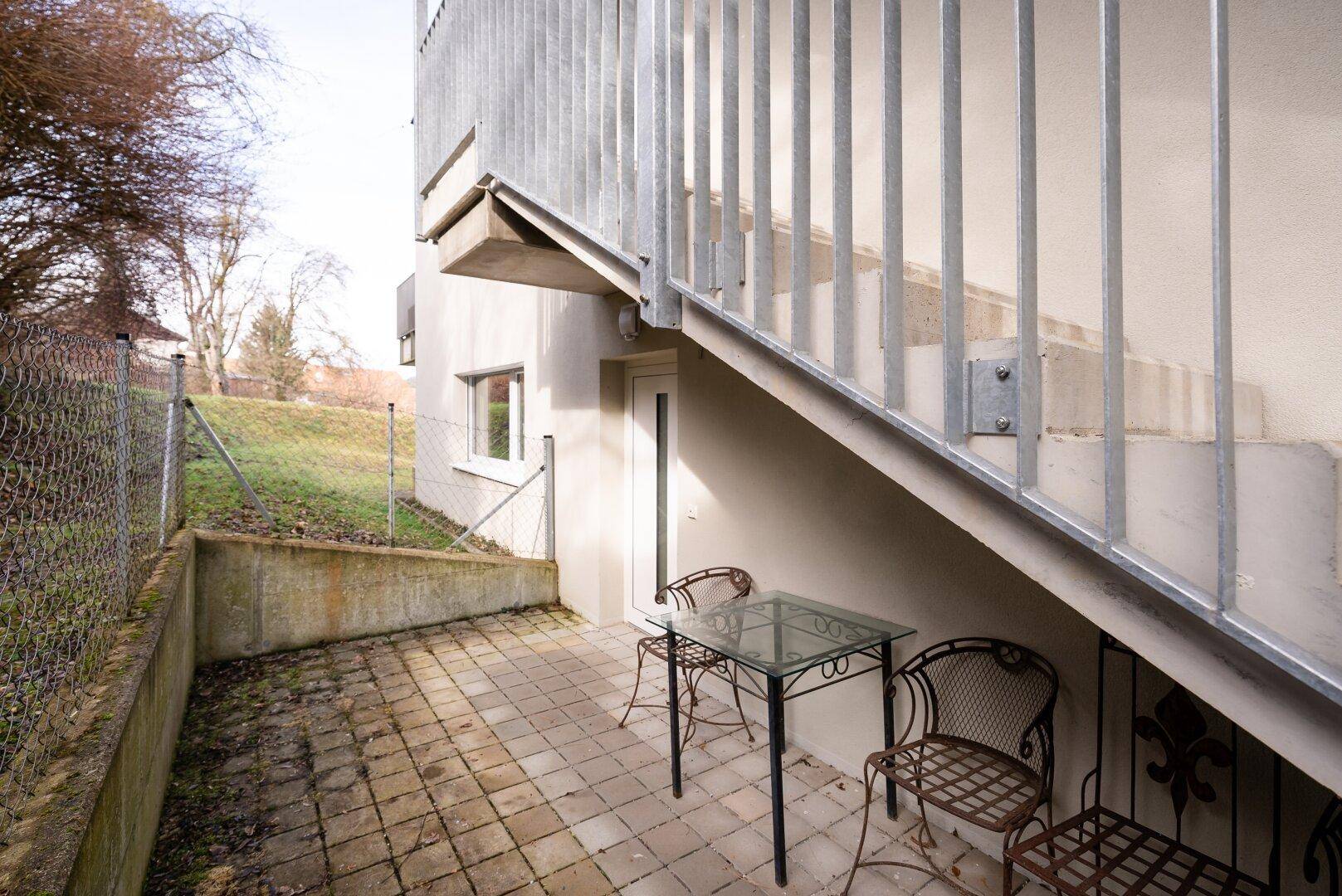 Kleine gepflasterte Terrasse unter einer Außentreppe mit Sitzgelegenheiten.