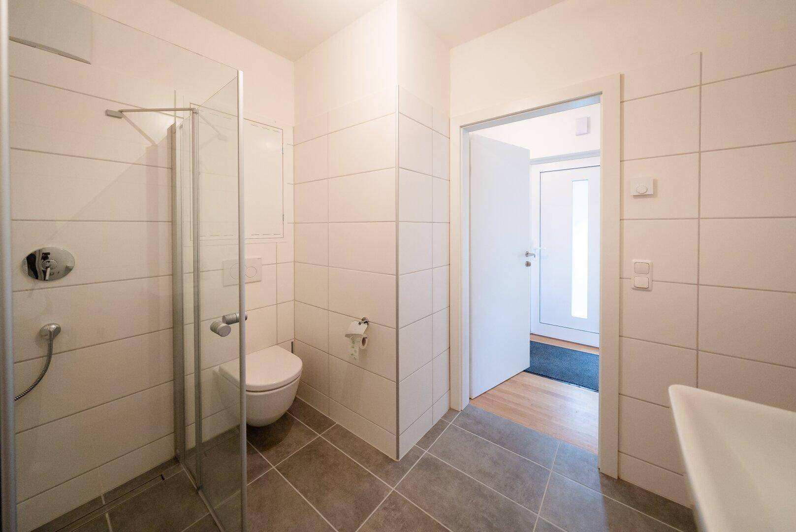 Modernes Badezimmer mit Duschkabine, wandhängendem WC und weißen Fliesen.
