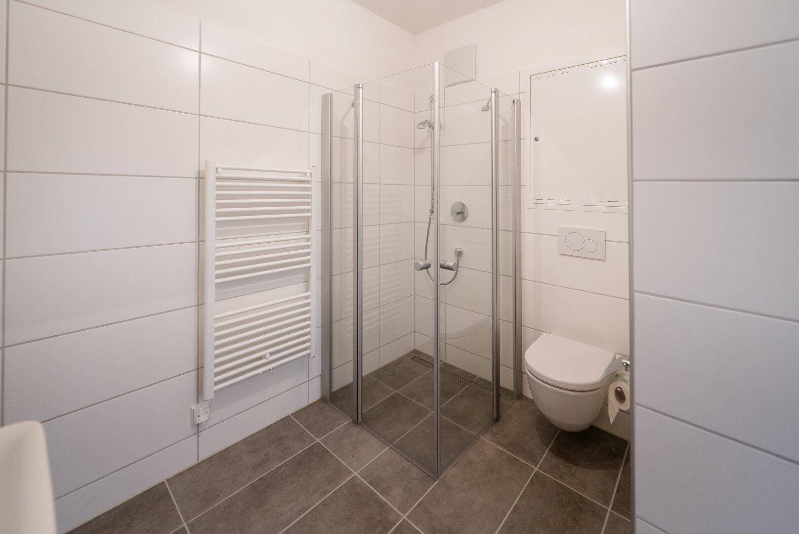 Helles Badezimmer mit Duschkabine, WC und beheiztem Handtuchhalter.