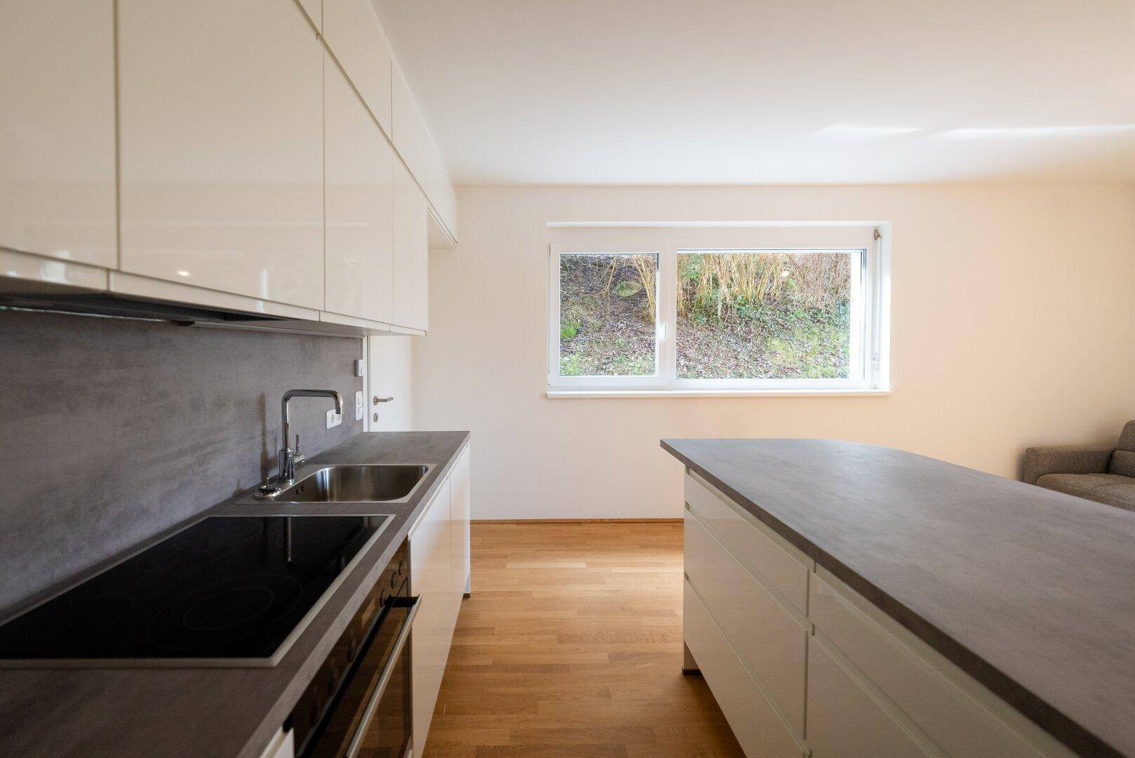 Moderne Küche mit weißer Hochglanzfront, grauer Arbeitsplatte und Induktionskochfeld.