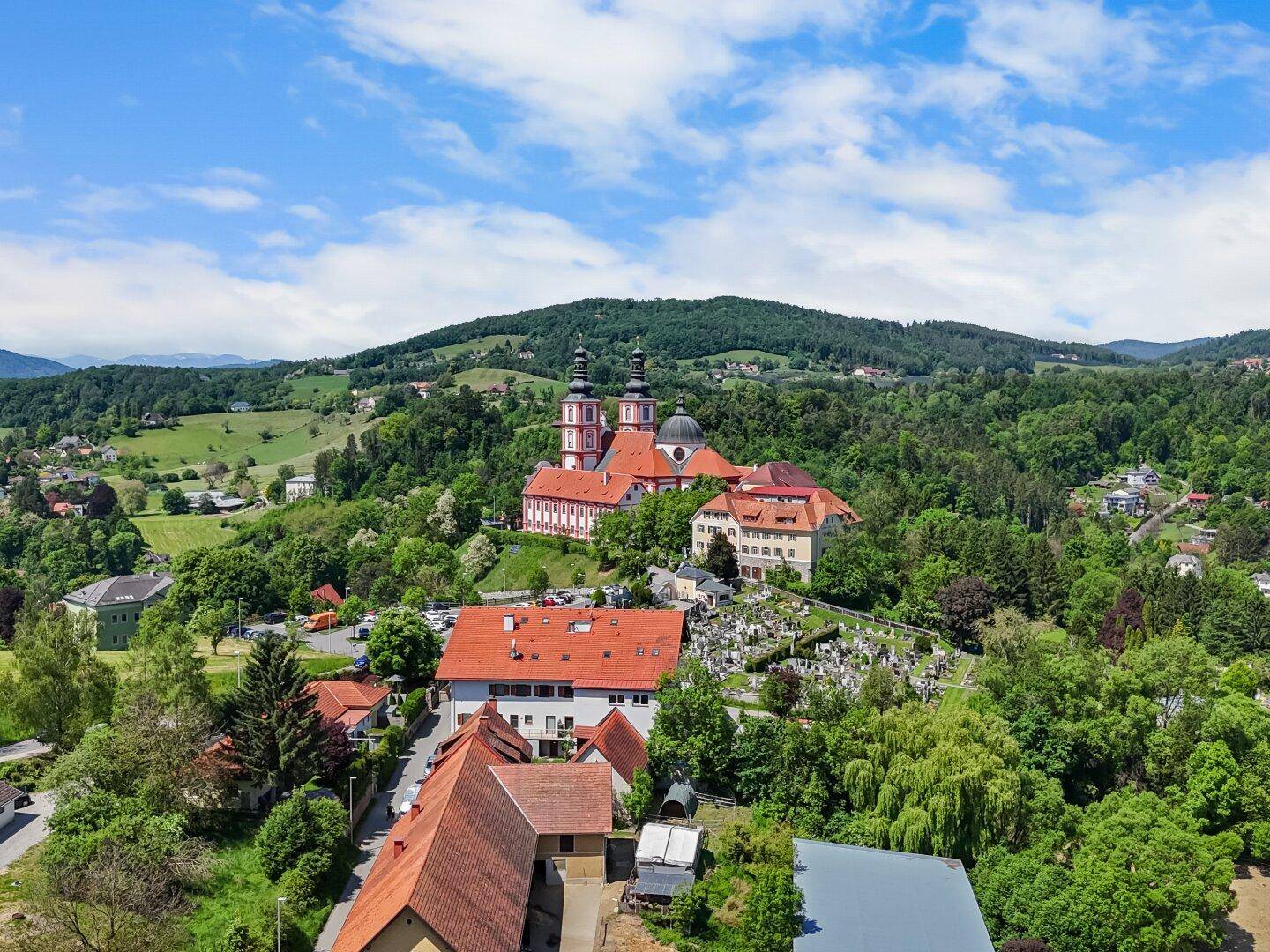 Panoramablick auf eine malerische Ortschaft mit historischer Kirche, umgeben von grünen Hügeln.