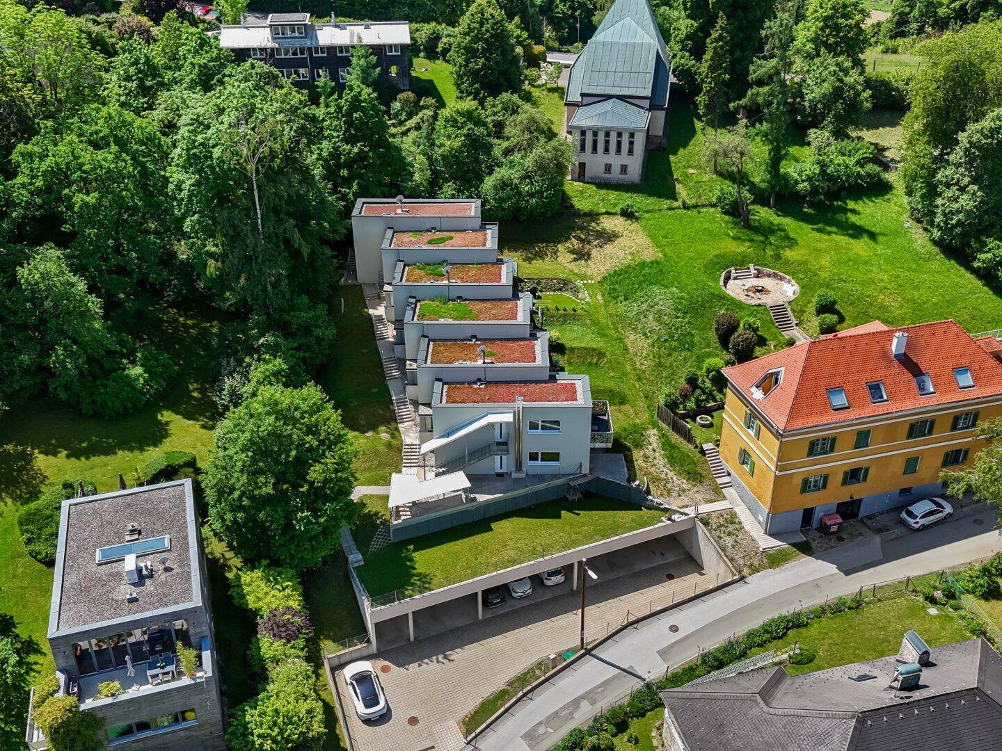 Weitläufige Luftaufnahme der modernen Wohnanlage mit viel Grün und einer Kirche im Hintergrund.