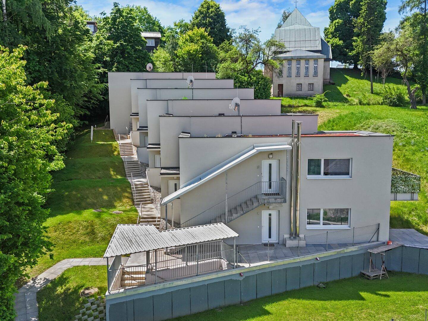 Ansicht der modernen Reihenhäuser mit Außentreppen und gepflegten Grünflächen.