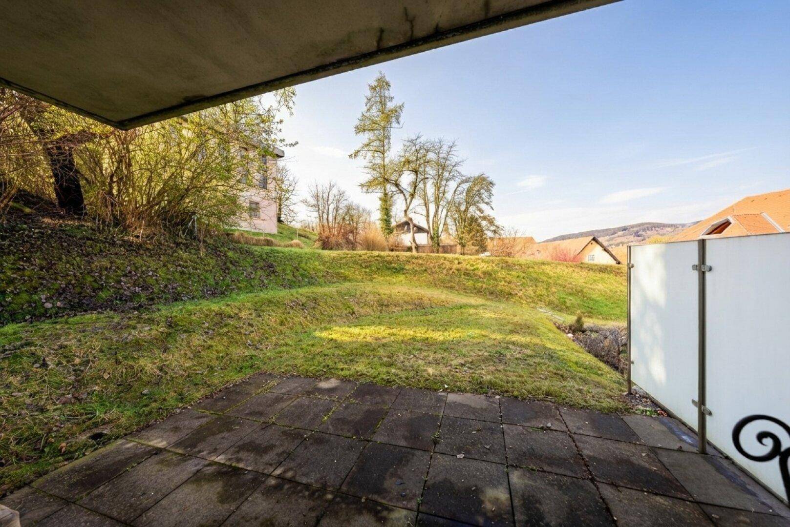Gepflasterte Terrasse mit Blick auf eine grüne Böschung und Bäume.