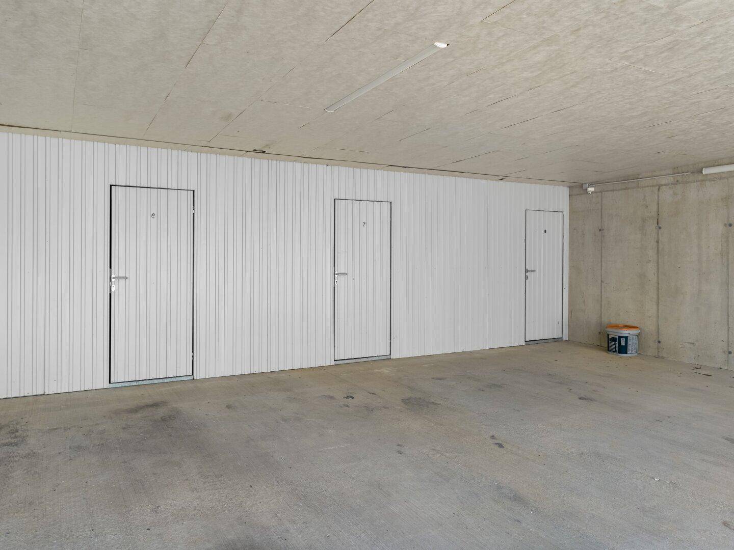 Geräumige Garage oder Abstellraum mit mehreren weißen Türen und Betonboden.