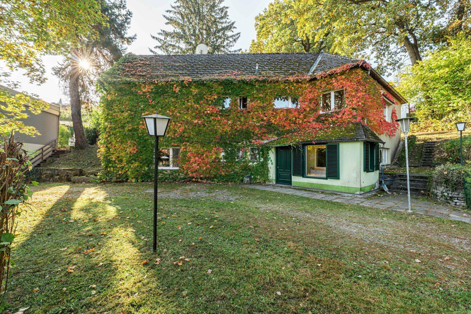 Vorderansicht des charmanten Hauses, vollständig mit herbstlichem Efeu bewachsen, umgeben von einem gepflegten Garten.