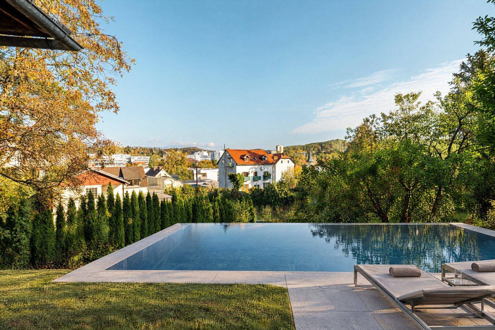 Luxuriöser Infinity-Pool mit Liegestühlen und Panoramablick über die Stadt und die grüne Umgebung.