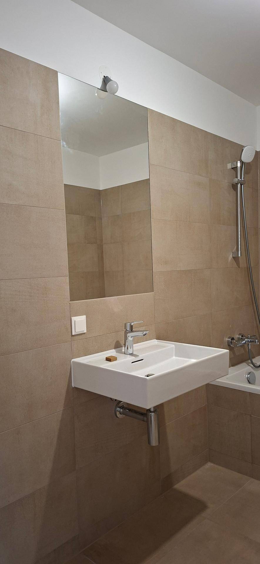 Modernes Badezimmer mit beigefarbenen Fliesen, Waschbecken und Duscharmatur über der Badewanne.