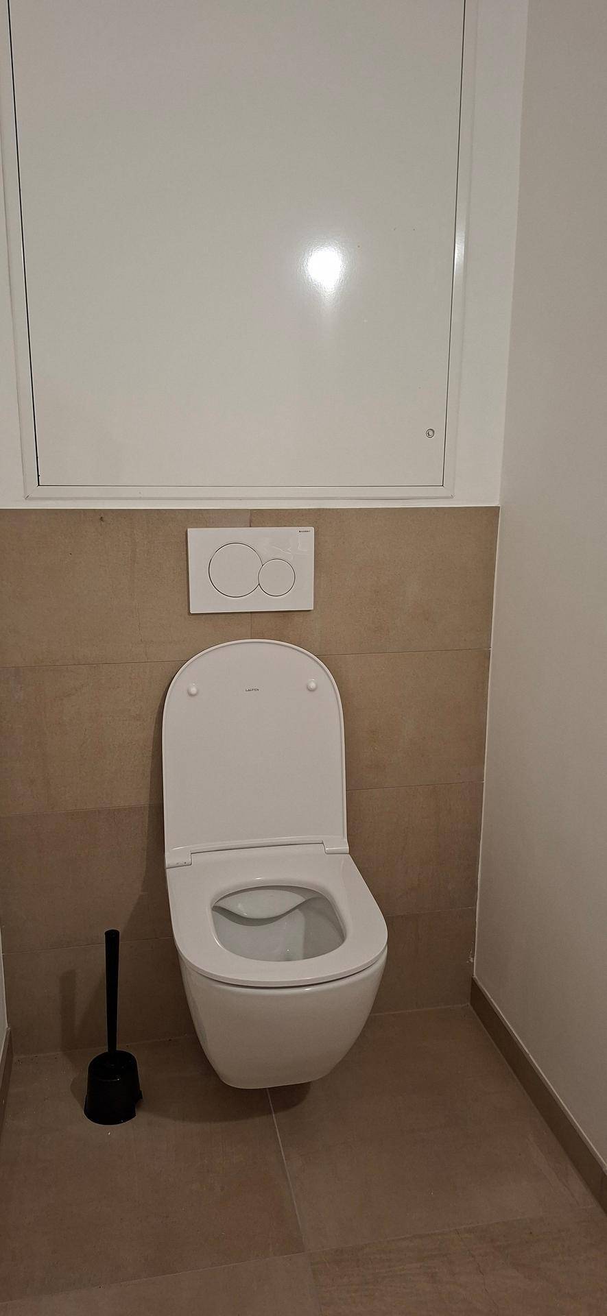Separates WC mit wandhängender Toilette und beigefarbenen Fliesen an den Wänden.