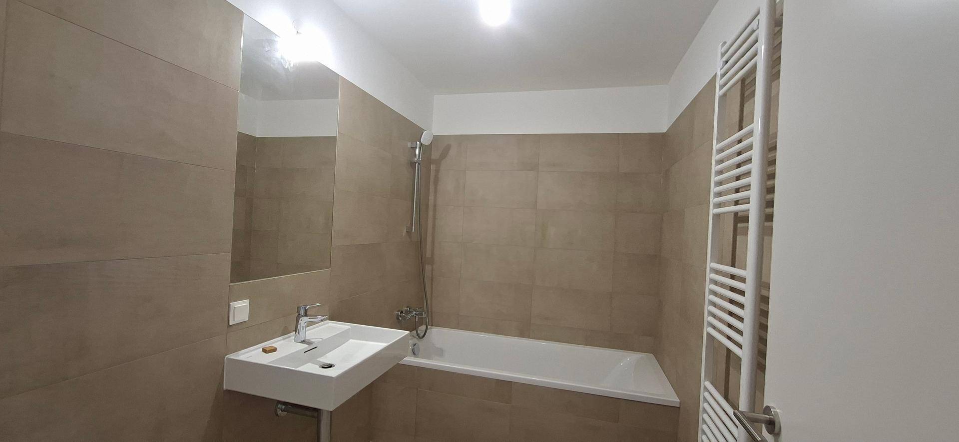 Helles Badezimmer mit Badewanne, Waschbecken, Spiegel und beheiztem Handtuchhalter.
