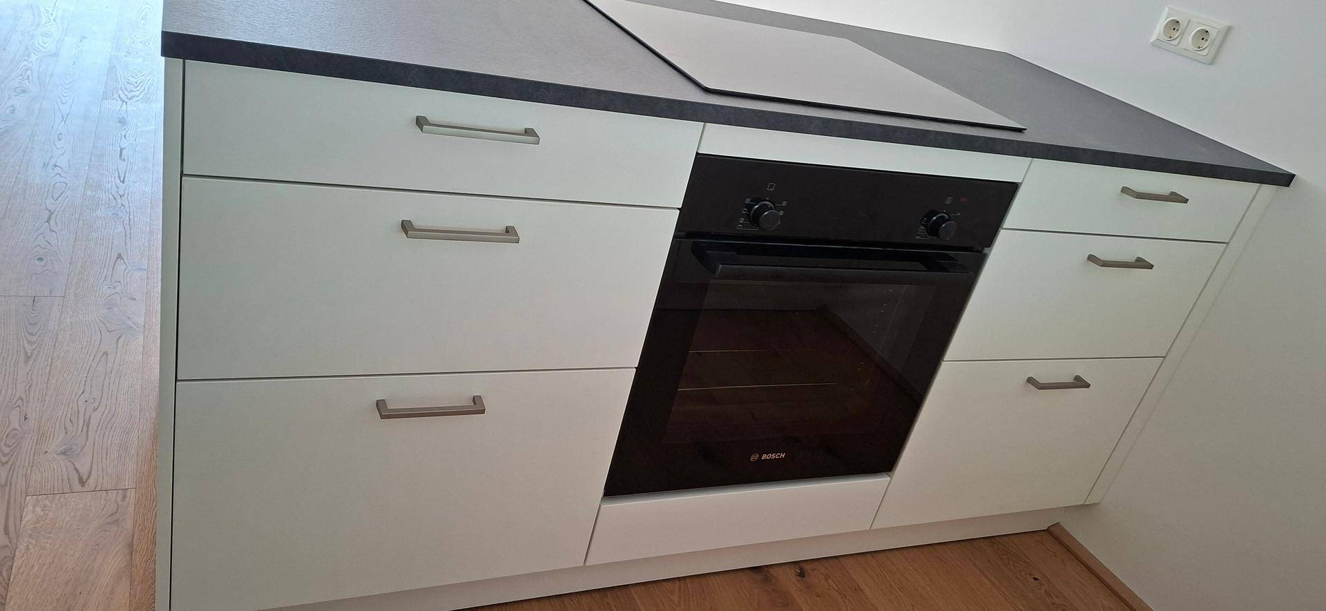 Integrierter Backofen und Induktionskochfeld in der modernen weißen Einbauküche.