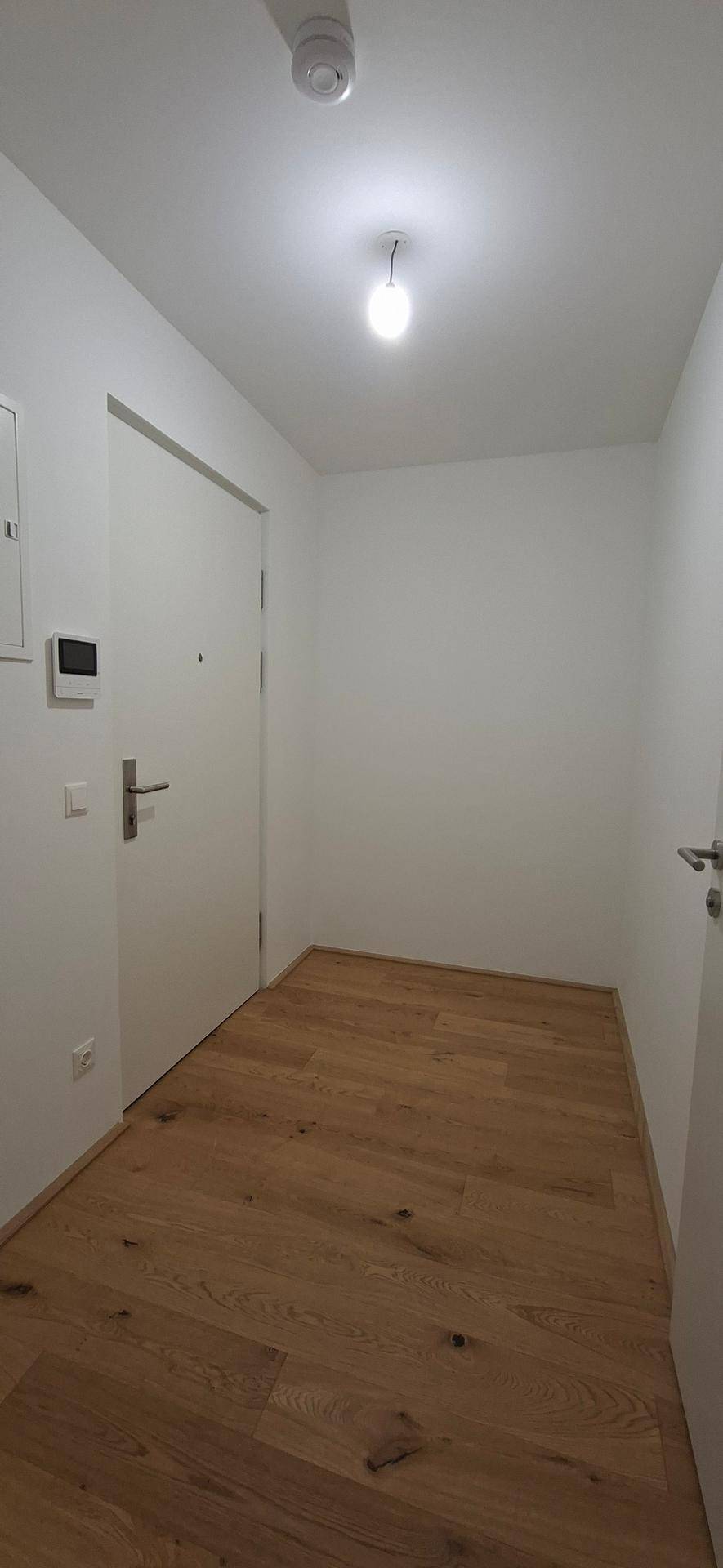 Heller Flur mit Holzboden und weißen Wänden, der den Eingangsbereich bildet.