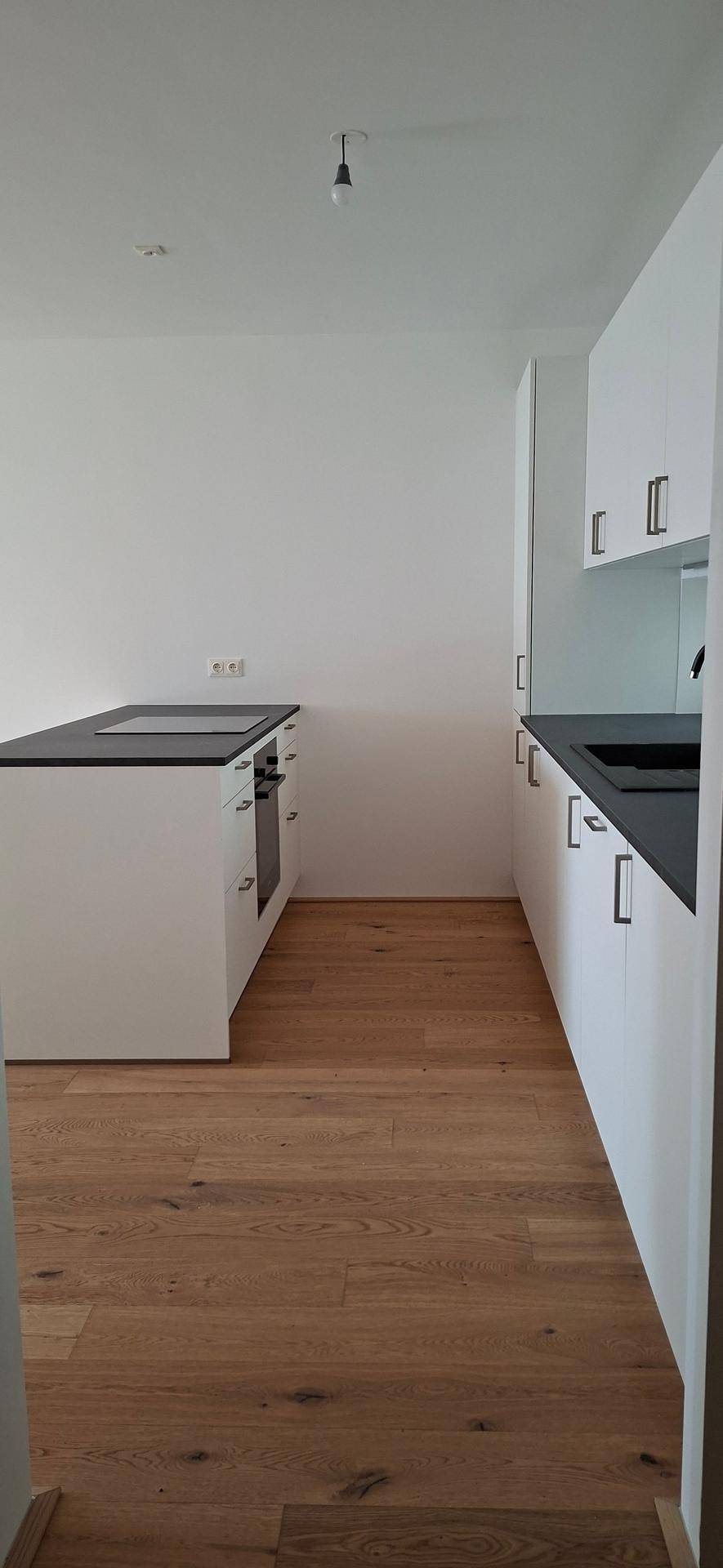 Geräumige Küche mit Holzboden, weißen Schränken und dunklen Arbeitsplatten in modernem Design.