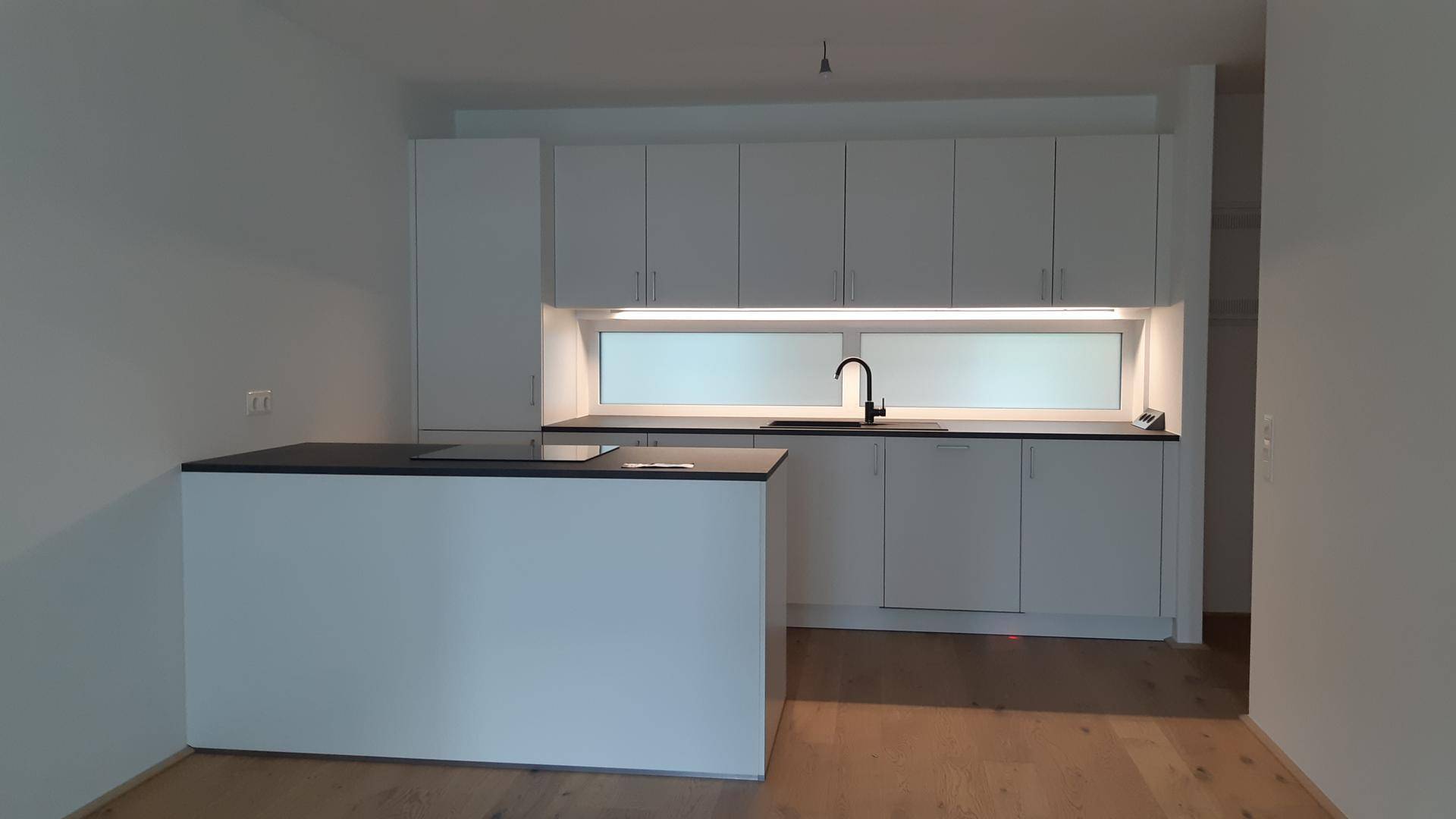 Moderne Einbauküche in Weiß mit dunkler Arbeitsplatte und integrierter Kücheninsel.