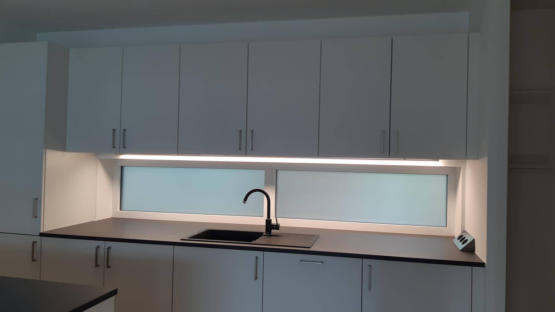 Detailansicht der modernen Küche mit Spülbecken, schwarzem Wasserhahn und beleuchteter Nische.