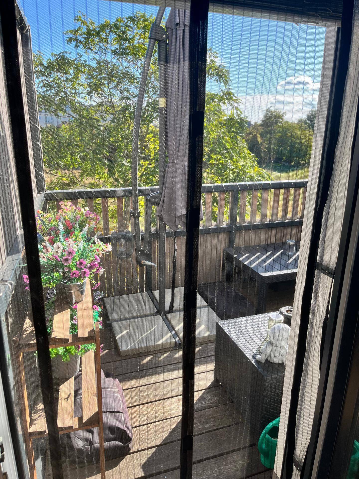 Geräumiger Balkon mit Sonnenschirm, Pflanzen und weitem Blick in die Natur.