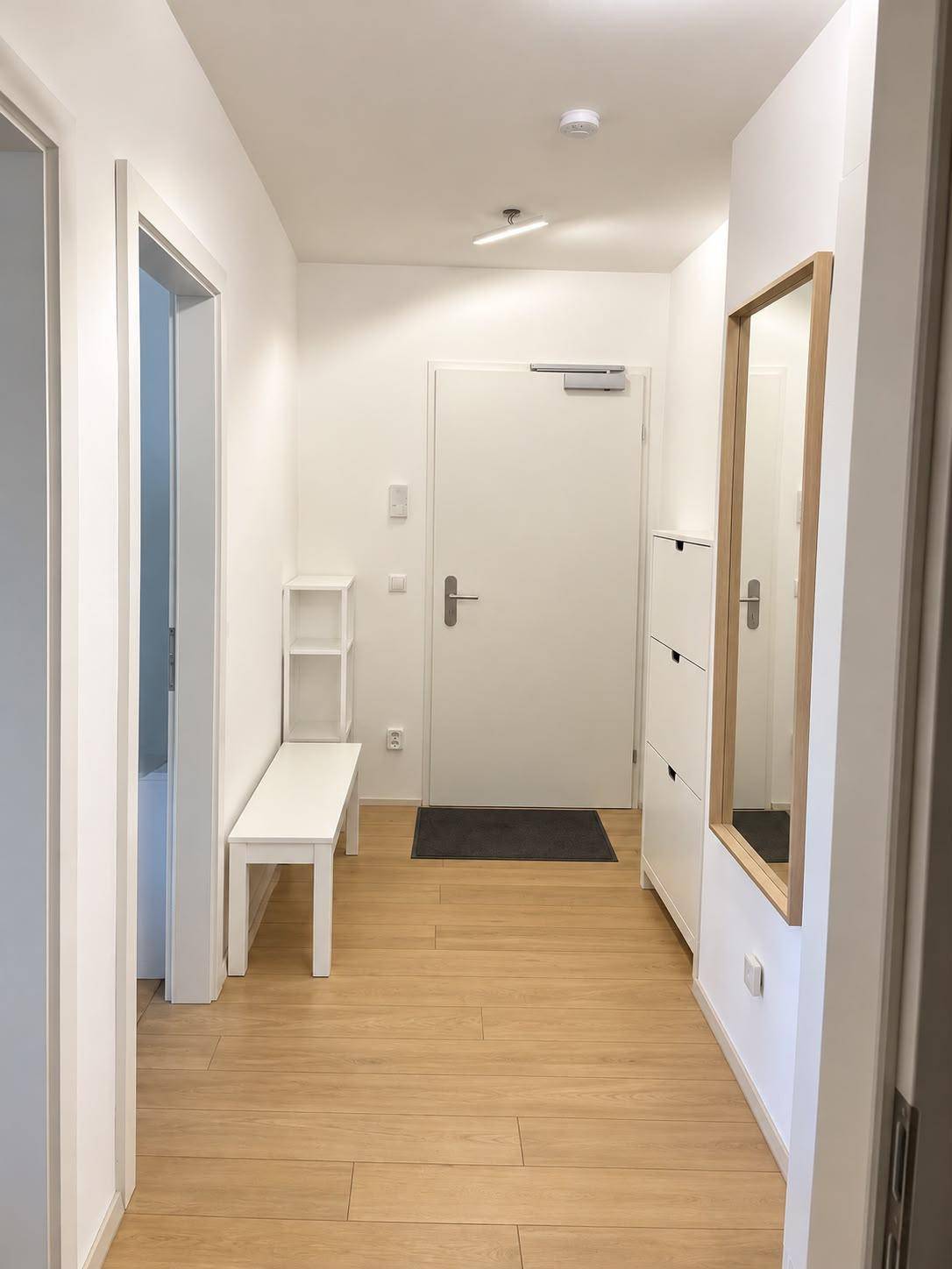 Heller Eingangsbereich mit Holzboden, Spiegel und weißer Schuhkommode.