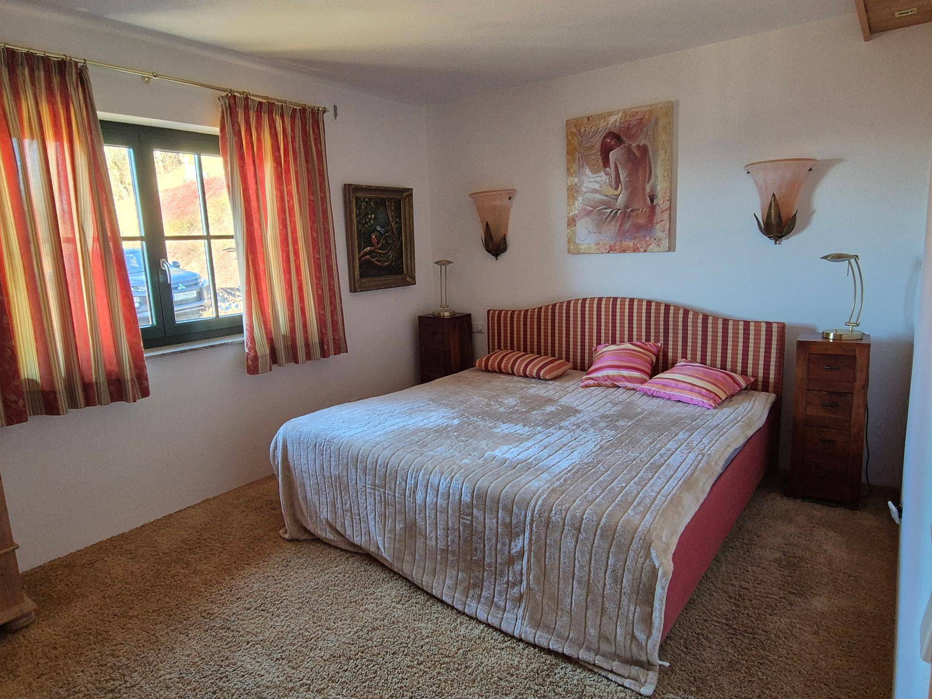 Gemütliches Schlafzimmer mit Teppichboden, Doppelbett und farbigen Vorhängen.
