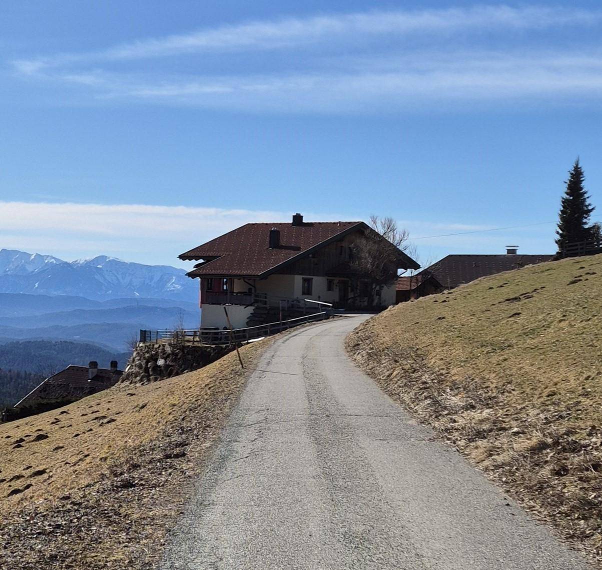 Haus auf einem Hügel mit Zufahrtsweg und weitem Blick auf die umliegende Berglandschaft.