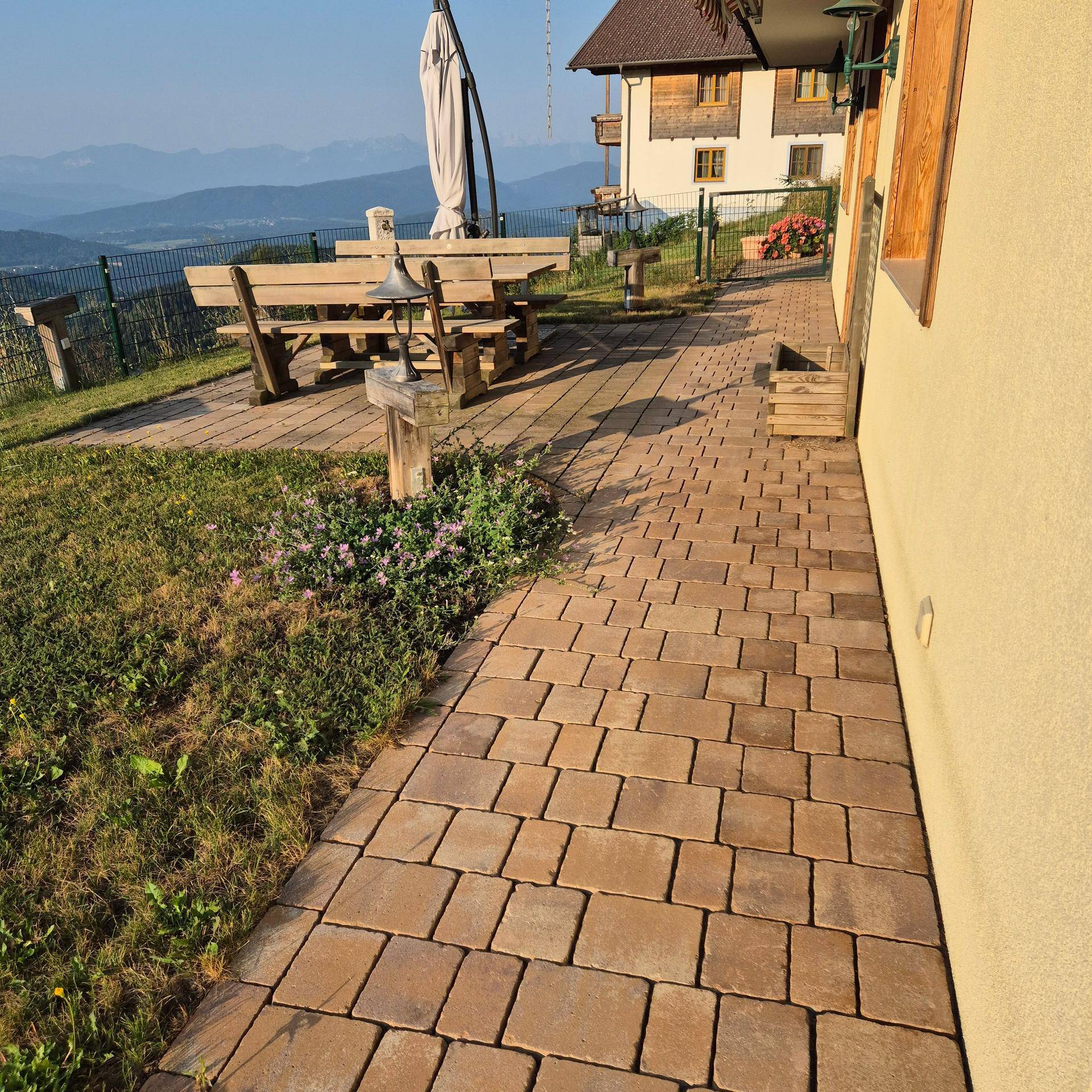 Gepflasterter Weg im Gartenbereich mit Sitzgelegenheiten und Blick auf die umliegende Natur.