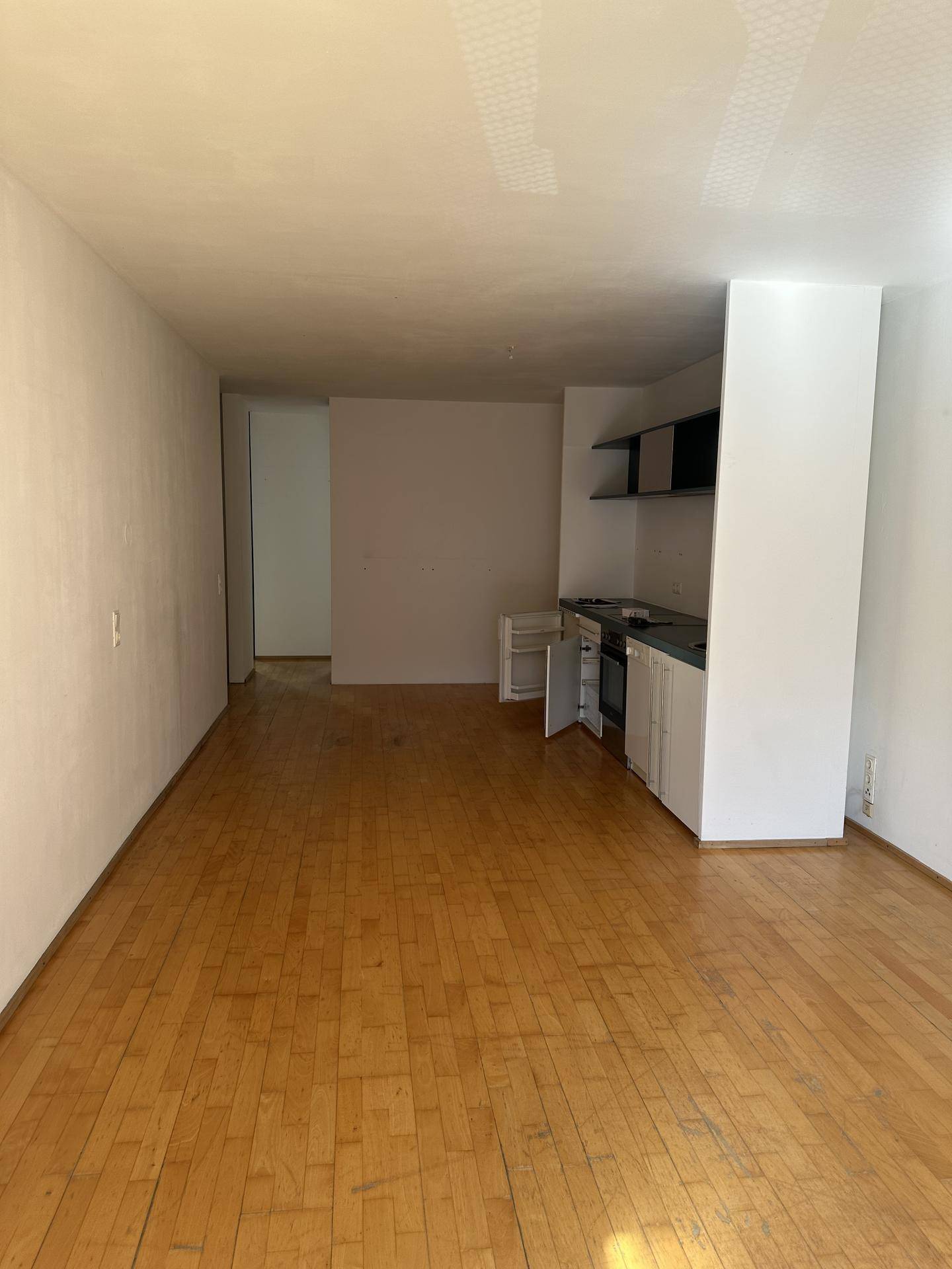 Langer Wohnbereich mit Küchenzeile und Holzboden, der vielseitige Gestaltungsmöglichkeiten bietet.