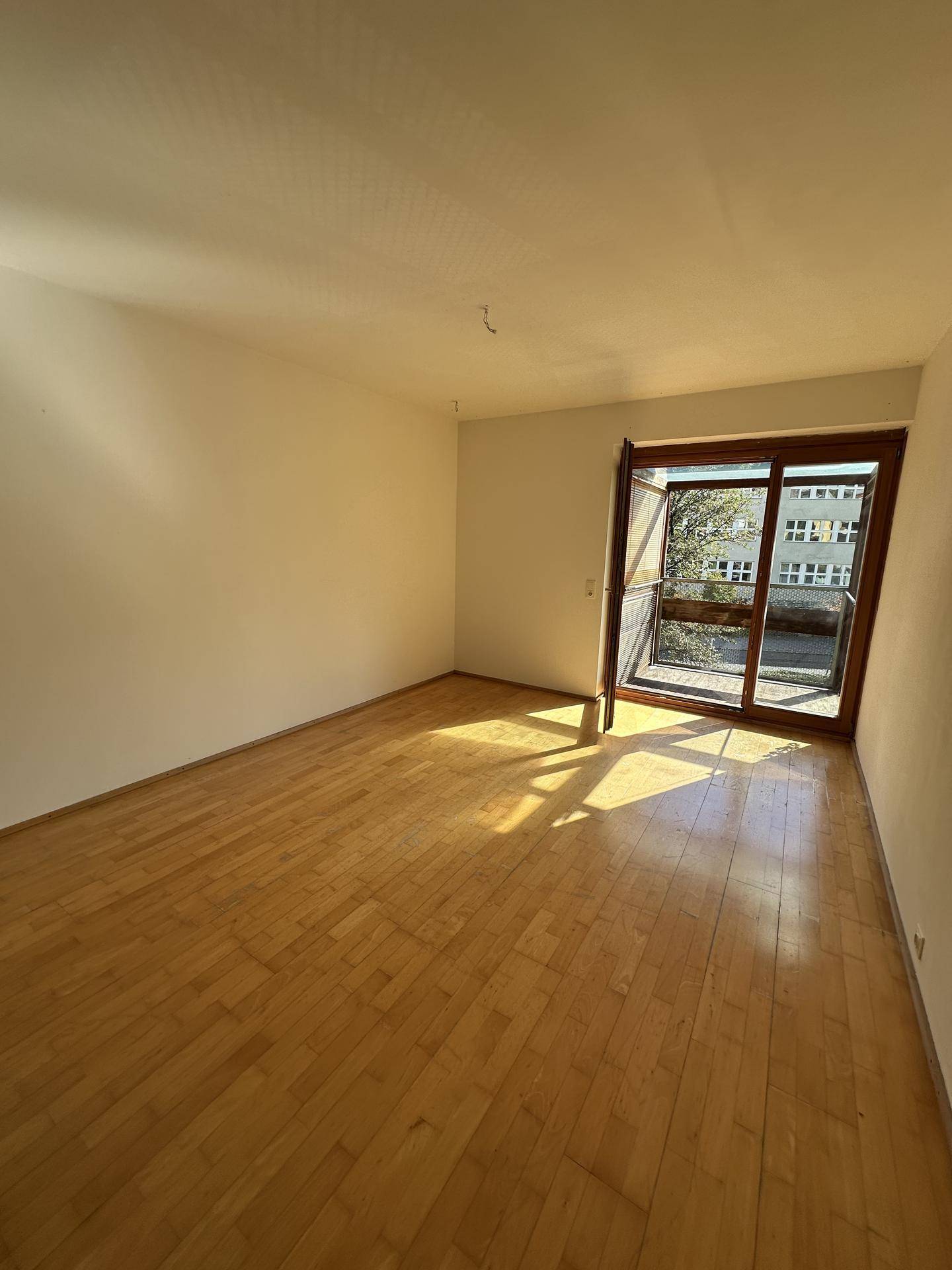 Geräumiges, helles Zimmer mit Parkettboden und großem Fenster, das viel Tageslicht hereinlässt.