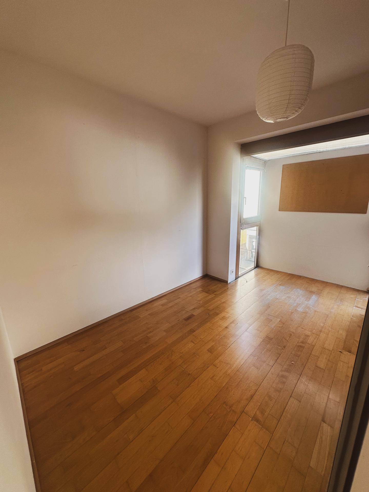 Helles Schlafzimmer mit Holzboden und großem Fenster, das viel Tageslicht hereinlässt.