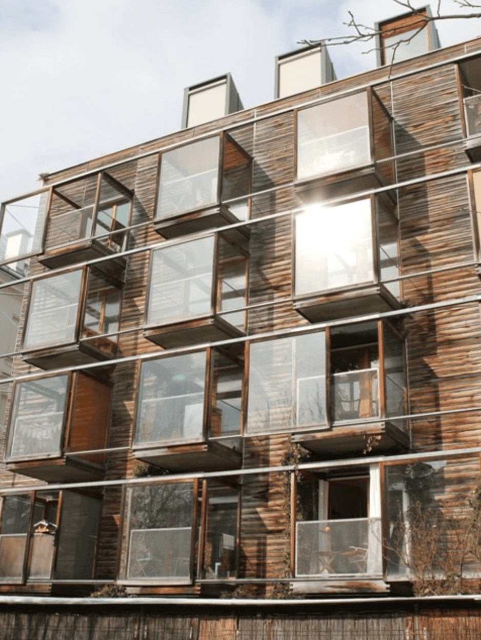 Moderne Fassade eines Gebäudes mit Holzverkleidung und zahlreichen verglasten Balkonen.