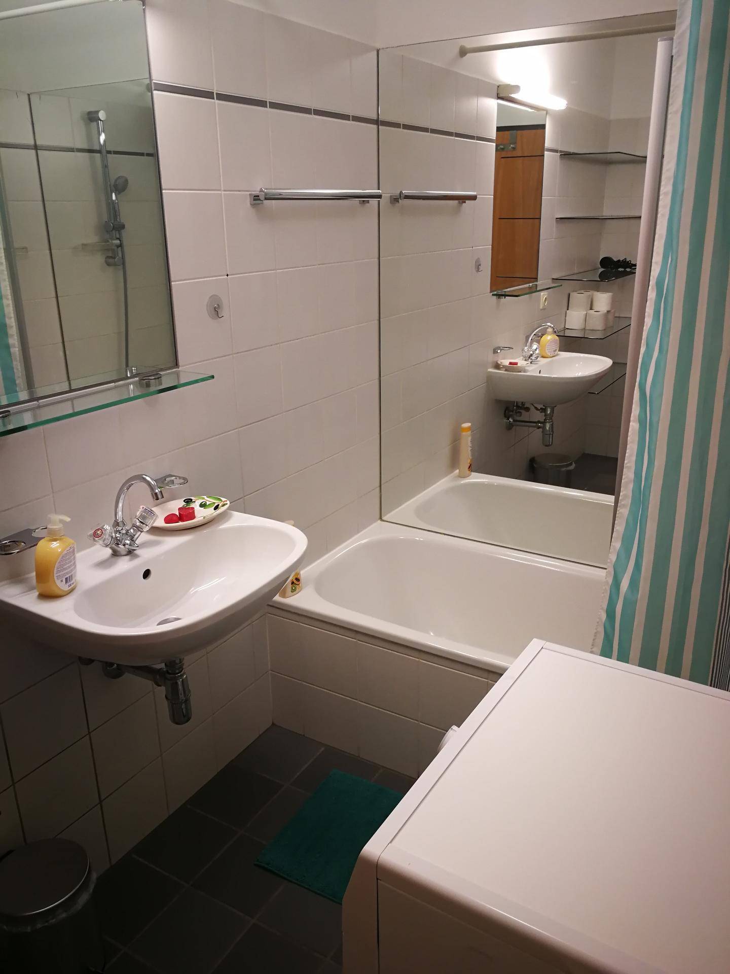 Funktionales Badezimmer mit Badewanne, Waschbecken und Waschmaschine, hell gefliest.
