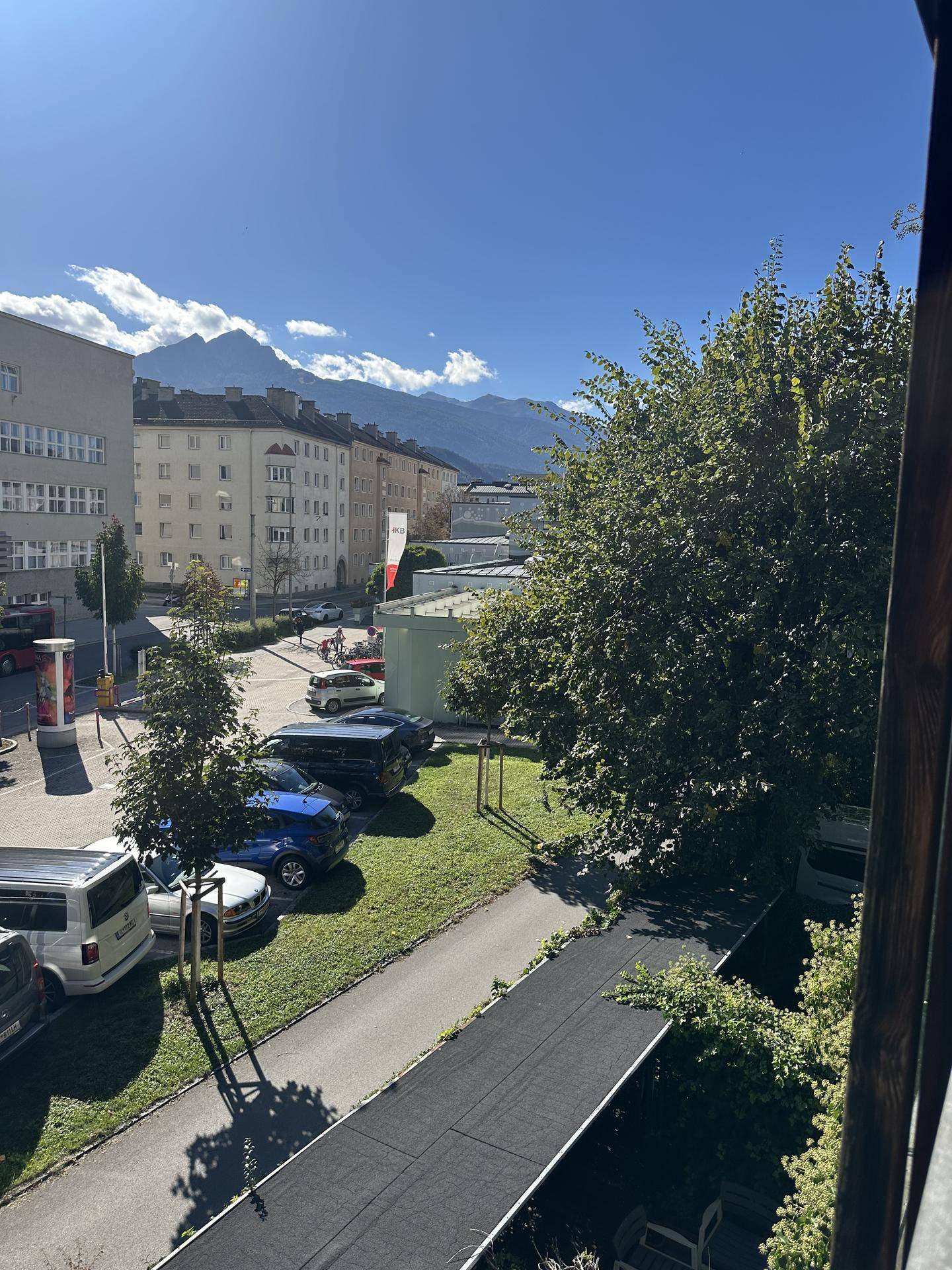 Panoramablick von der Wohnung auf die Stadt, grüne Bäume und die majestätischen Berge im Hintergrund.