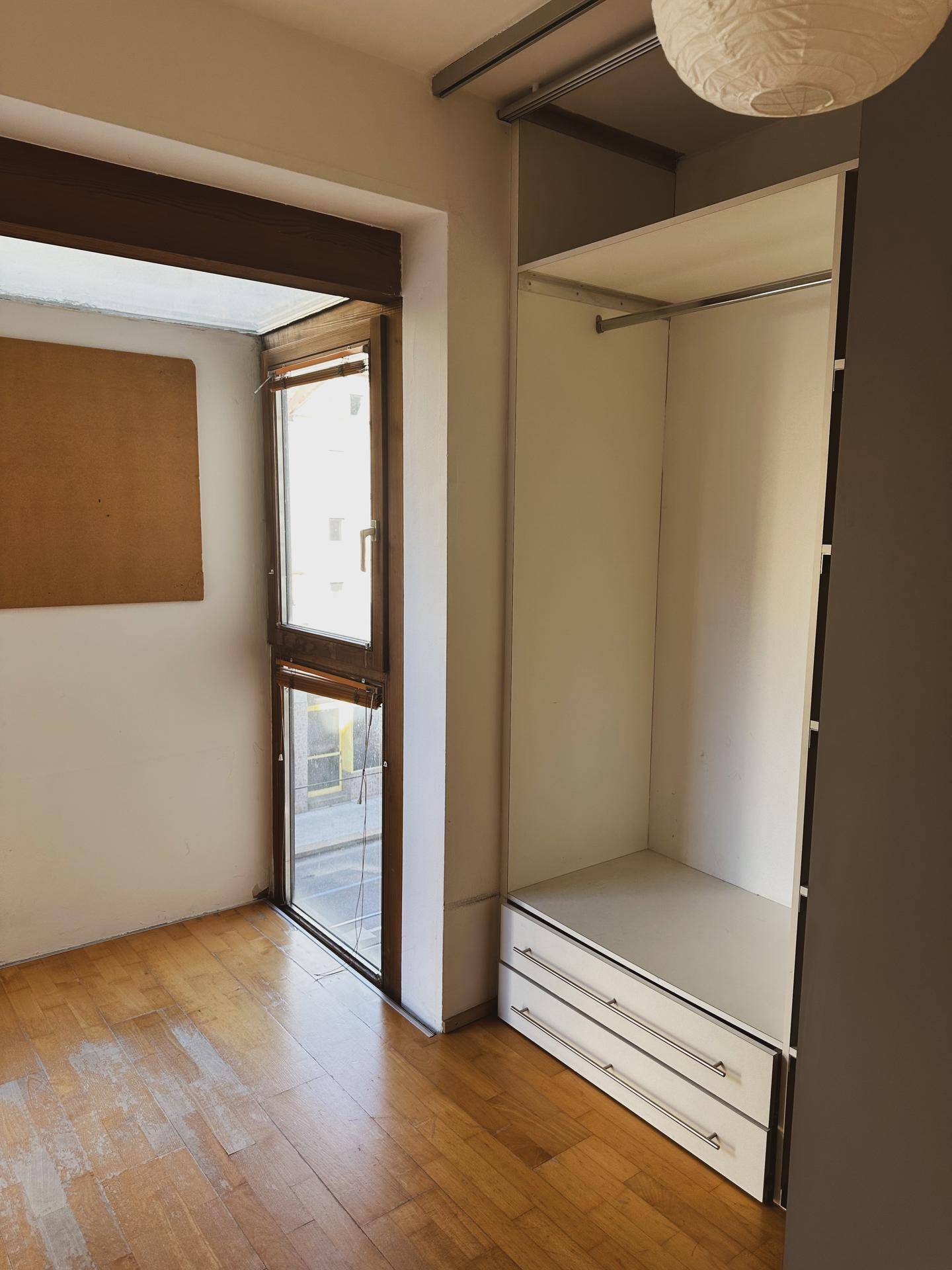 Schlafzimmer mit Einbauschrank, Holzboden und direktem Zugang zu einem sonnigen Balkon.