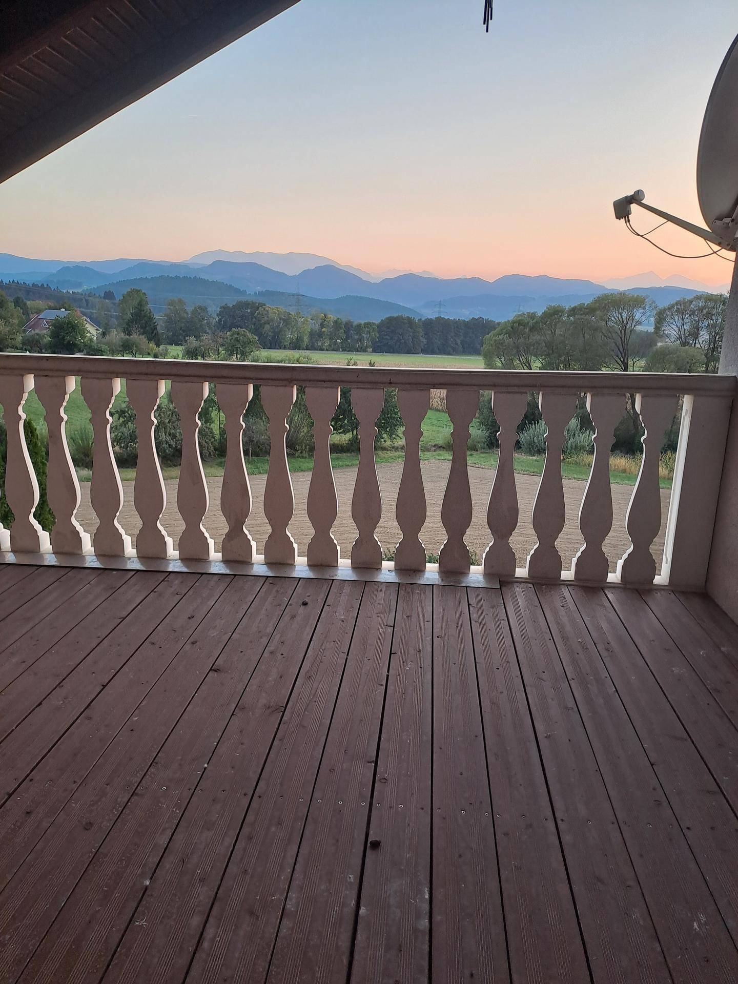 Geräumiger Holzbalkon mit weißem Geländer und weitem Blick auf die umliegende Berglandschaft.