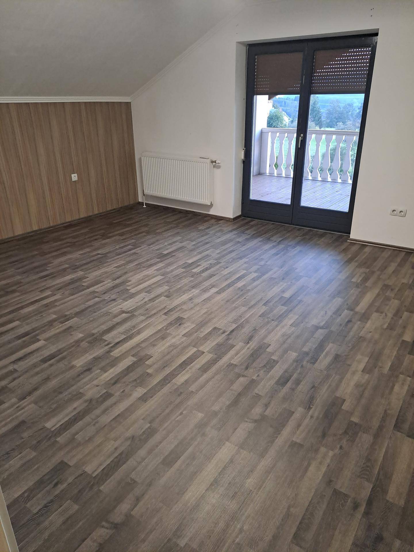 Geräumiges Zimmer mit Holzwandverkleidung, Laminatboden und Zugang zu einem Balkon.