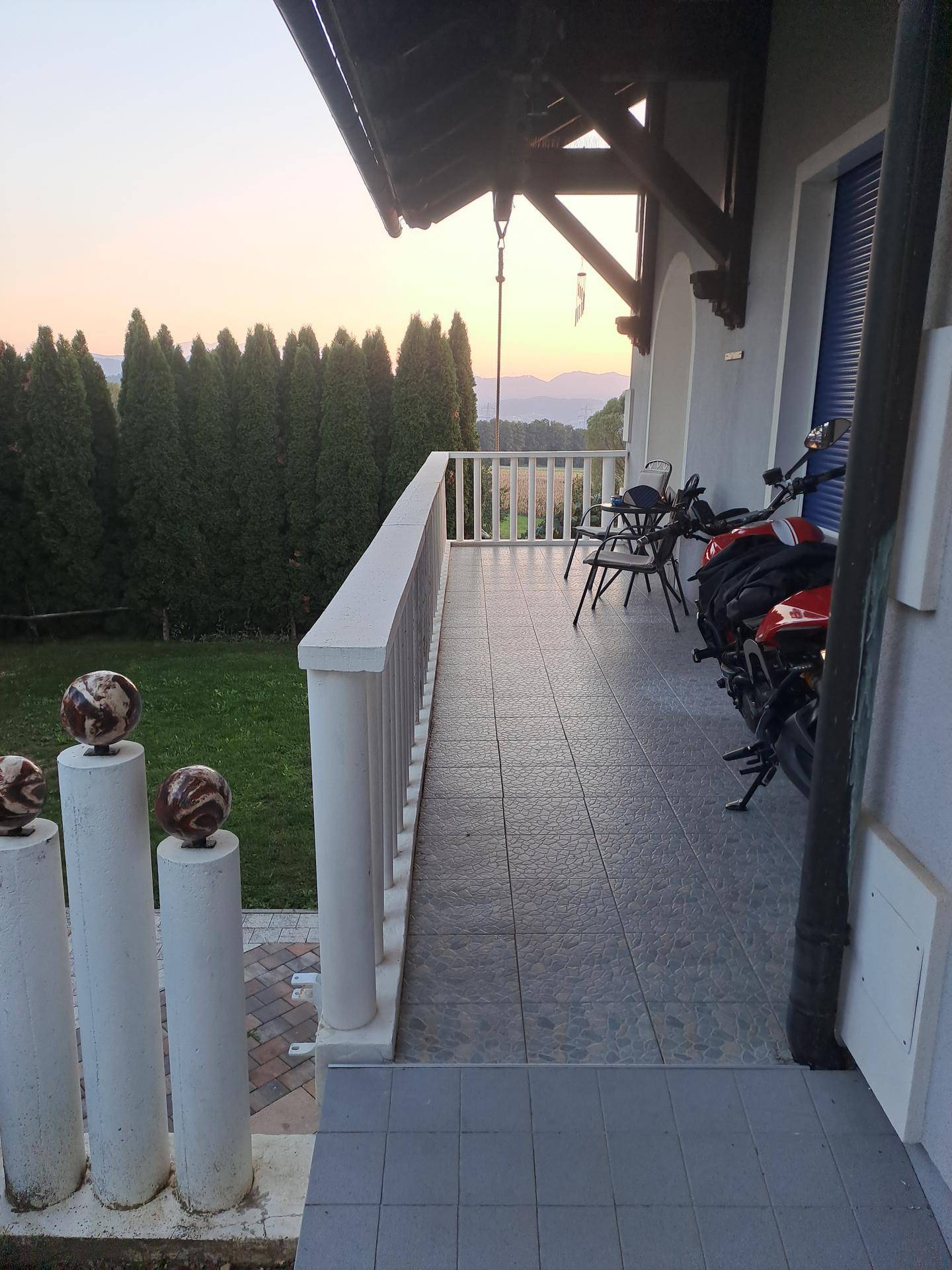 Balkon mit Fliesenboden, weißem Geländer und Sitzgelegenheiten, mit Blick in die Ferne.