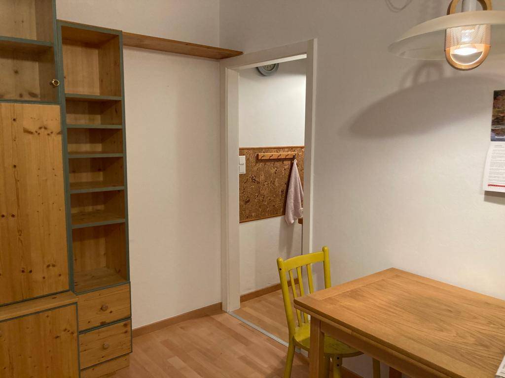 Essbereich mit Holztisch, gelbem Stuhl und Zugang zu einer weiteren Räumlichkeit.