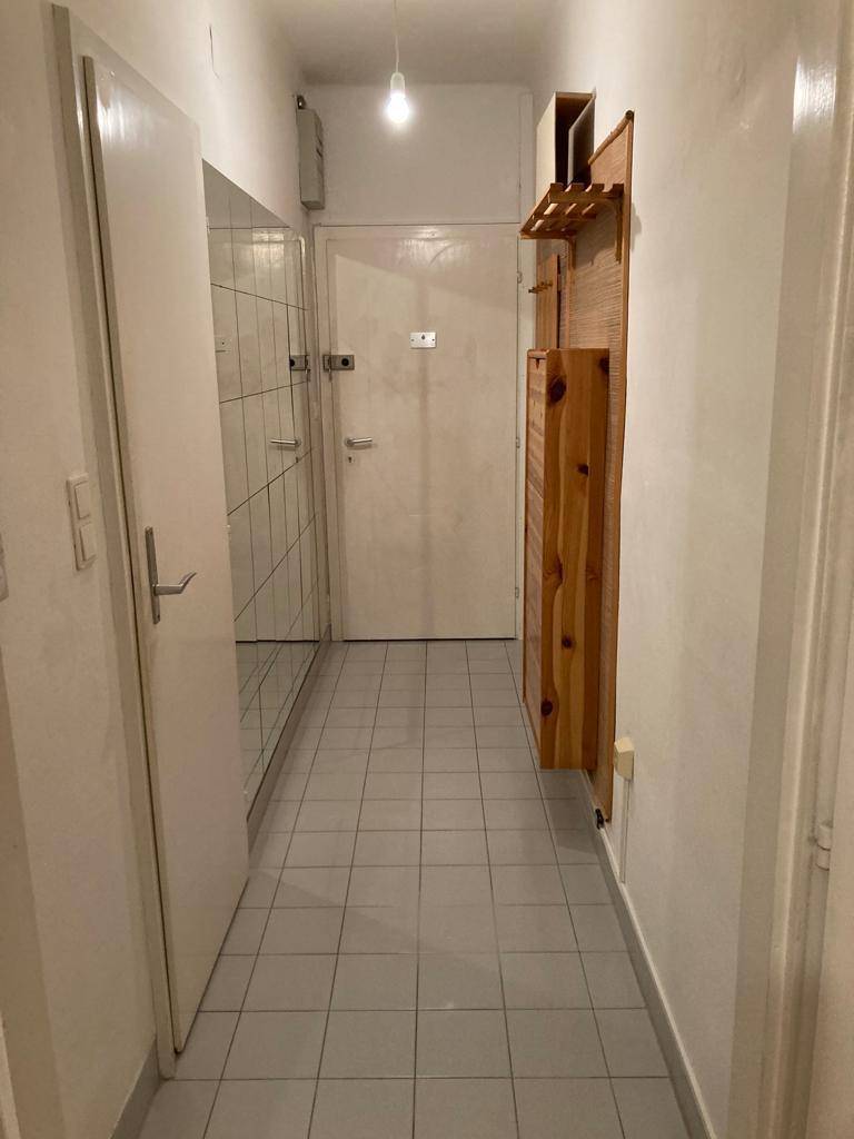 Heller Flur mit grauen Fliesen, weißen Wänden und praktischer Holzgarderobe.