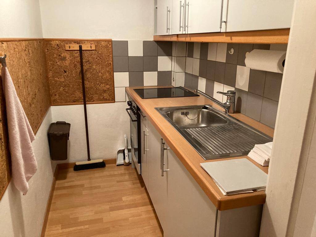 Kleine Küchenzeile mit weißen Schränken, Holztheke und kariertem Fliesenspiegel.