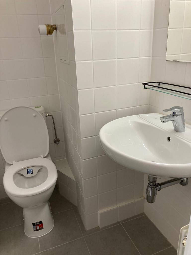 Funktionales Badezimmer mit WC, Waschbecken und Spiegel, komplett gefliest.