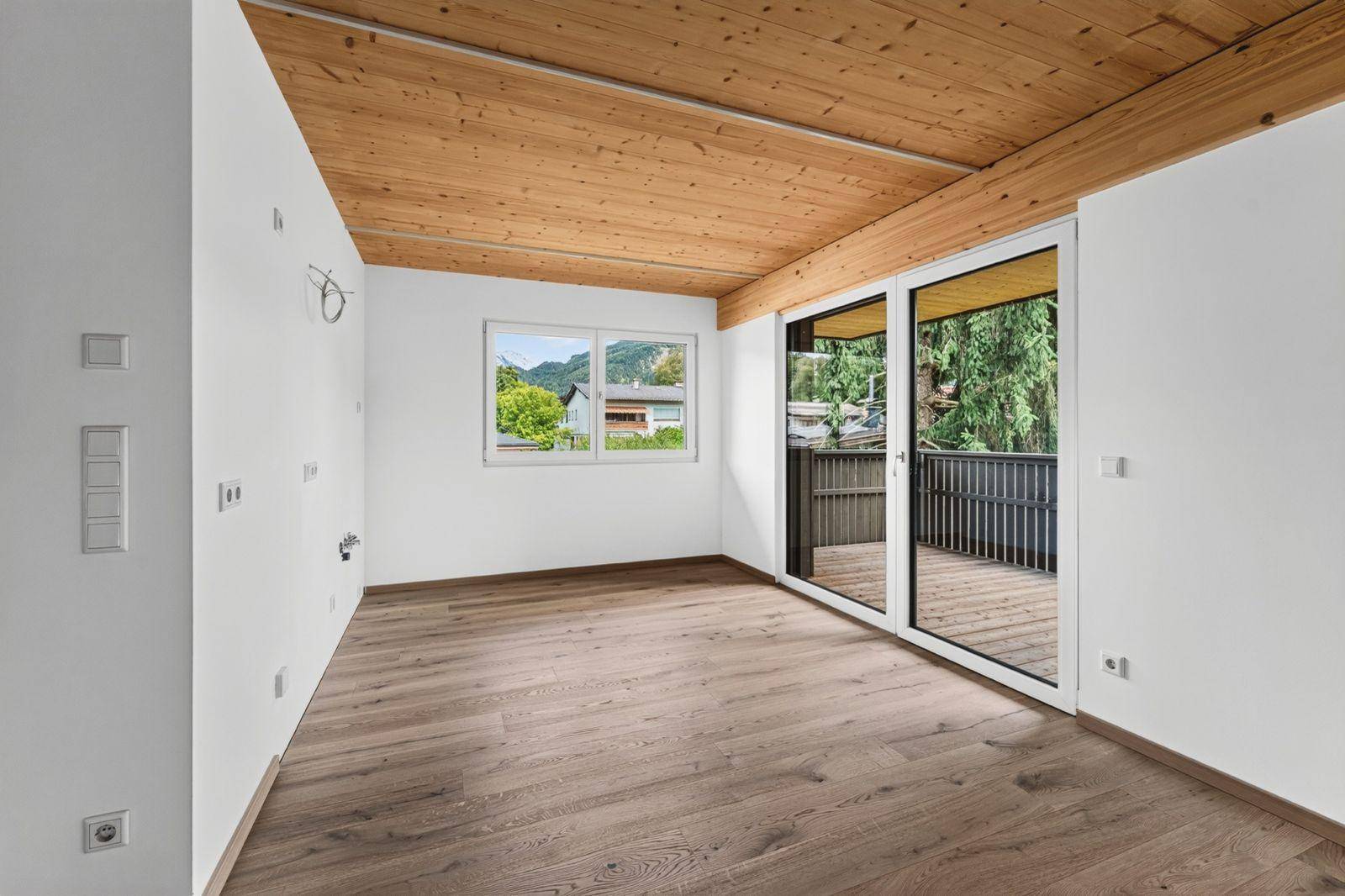 Heller, unmöblierter Raum mit Holzboden, Holzdecke und großem Zugang zum Balkon.
